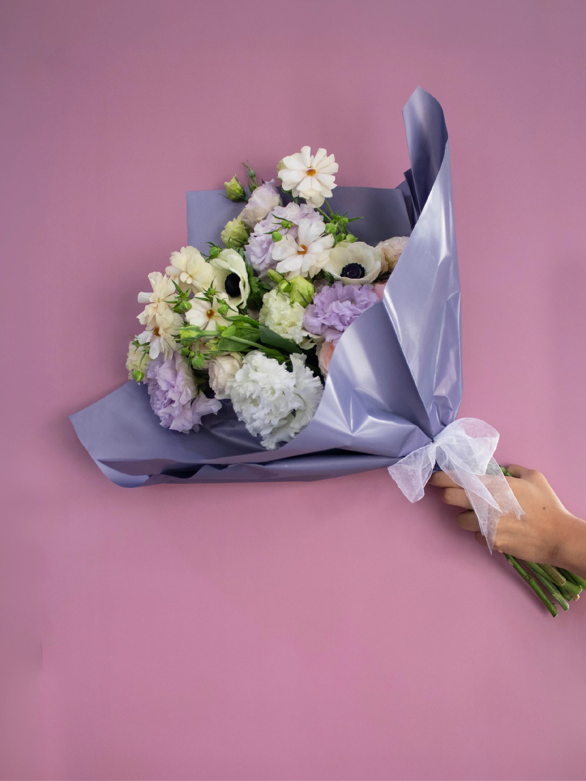 Bouquet of flowers wrapped in purple paper against a pink background.