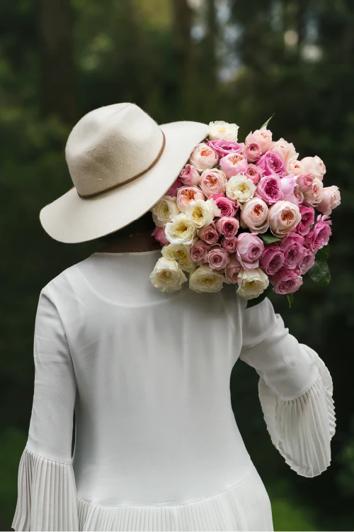 Person wearing a white hat and holding a large bouquet of pink and white garden roses against a blurred natural background.
#color_garden #detail