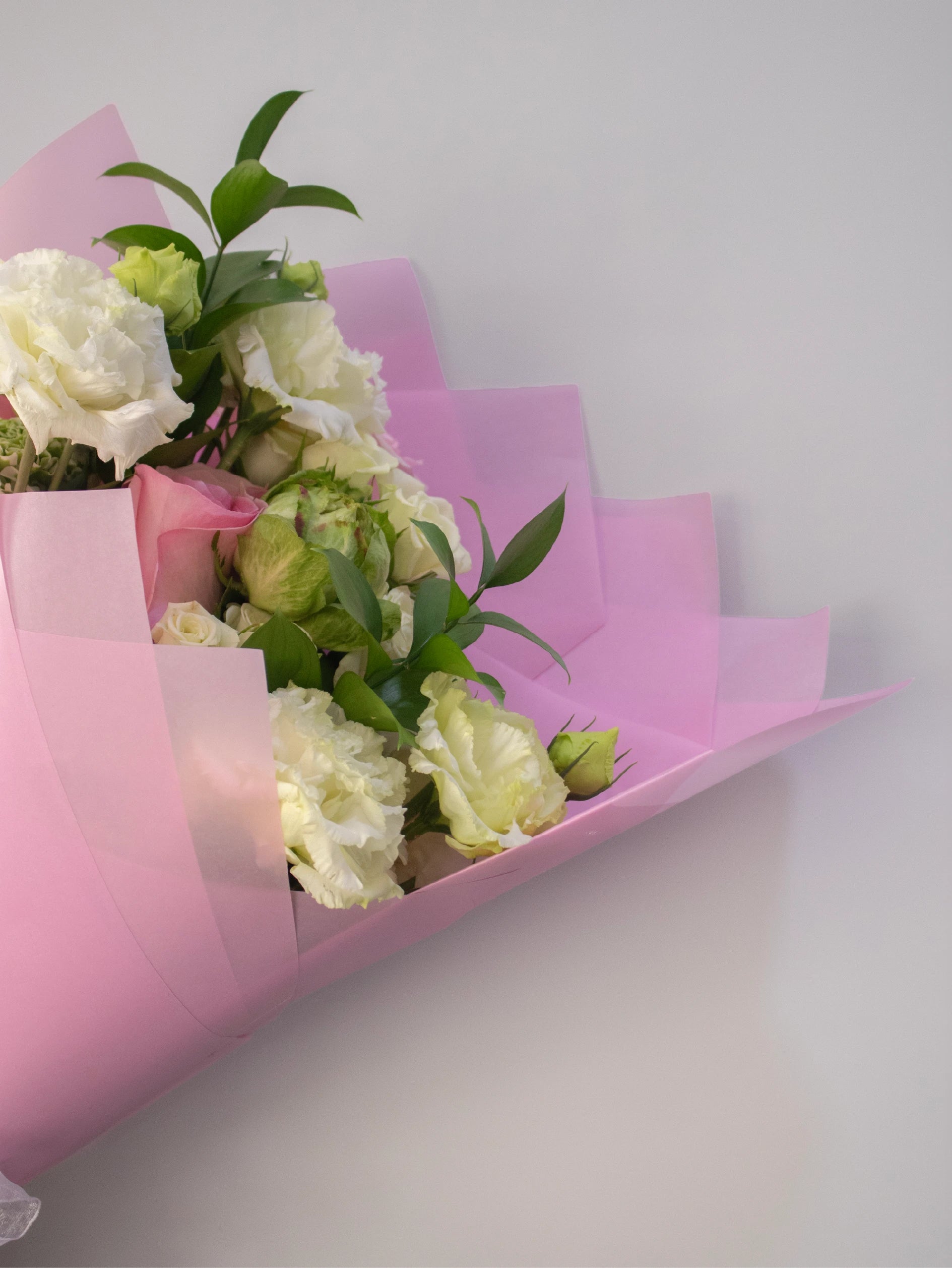Bouquet of flowers wrapped in pink paper on a light gray background.